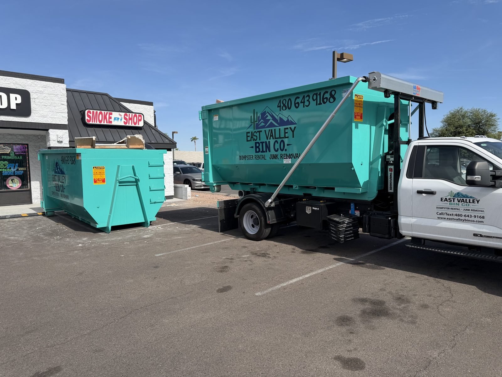 East Valley Bin Co. branded truck and roll-off dumpsters servicing a commercial storefront in the East Valley, Arizona