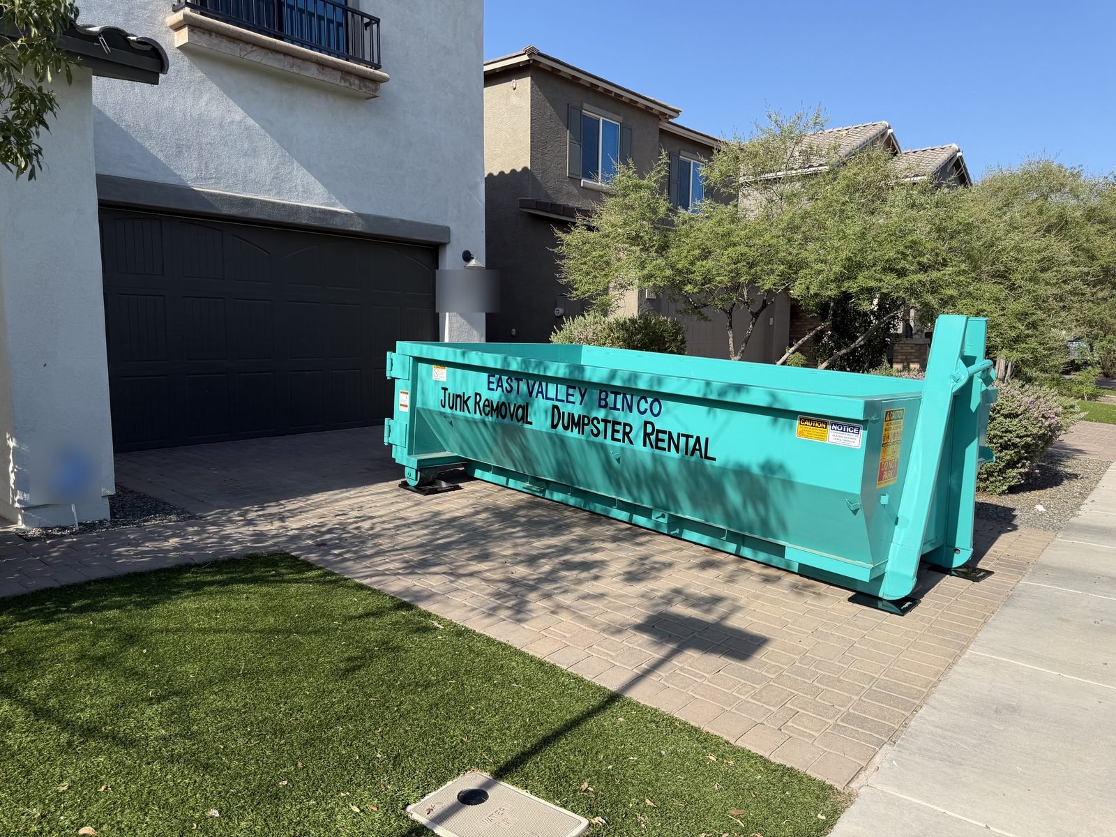 Branded teal East Valley Bin Co. dumpster placed on a residential paver driveway